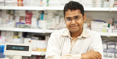 A male pharmacist stood with his arms crossed in front of medication shelves
